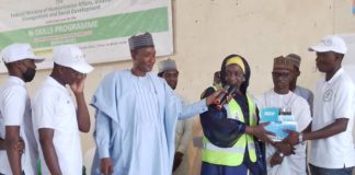 From left Alhaji Hashim Abubakar,SA to the President Dr Mahmoud Nasir, the representative of the Honourable Minister of Humanitarian Affairs Disaster Management and the Coordinator Commission for Refugees and Internally Displaced Persons Hajiya Lube Gusau handing a starter pack to a beneficiary during the closing ceremony of NSkills Kano State 27th April, 2022.