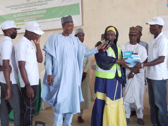 IMG-20220428-WA0014 From left Alhaji Hashim Abubakar,SA to the President Dr Mahmoud Nasir, the representative of the Honourable Minister of Humanitarian Affairs Disaster Management and the Coordinator Commission for Refugees and Internally Displaced Persons Hajiya Lube Gusau handing a starter pack to a beneficiary during the closing ceremony of NSkills Kano State 27th April, 2022.