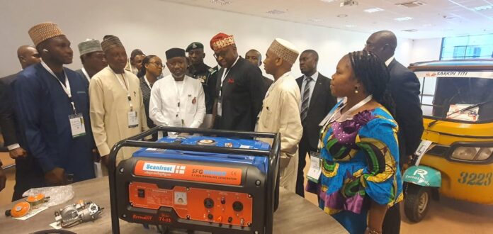 IMG-20231107-WA0054 The Minister (3rd left) flanked by other dignitaries listening to presentation on how Liquefied Petroleum Gas (LPG) can power Four Stroke Engine Tricycle and Petro Generator while inspecting various Exhibition Stands at the ongoing 13th LPGAS Conference and Exhibition in Abuja.