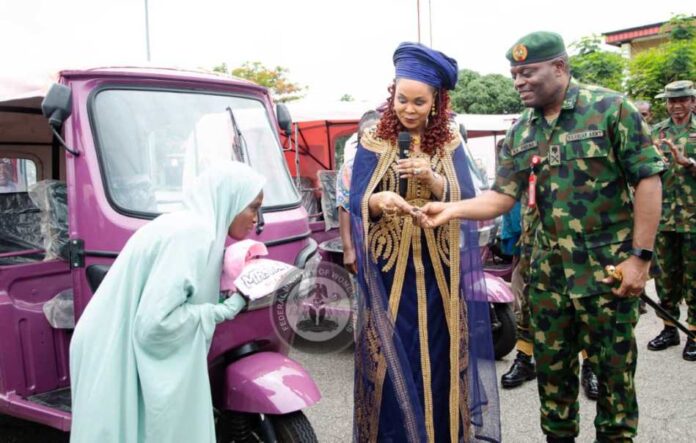 Pink Riders Tricycle Scheme1 Honourable Minister of Women Affairs presentating the keys, Pink Riders' T-shirt, and cap to one of the beneficiaries. To her left is the Commander, Army Headquarters Garrison, Abuja, Major General Isoni